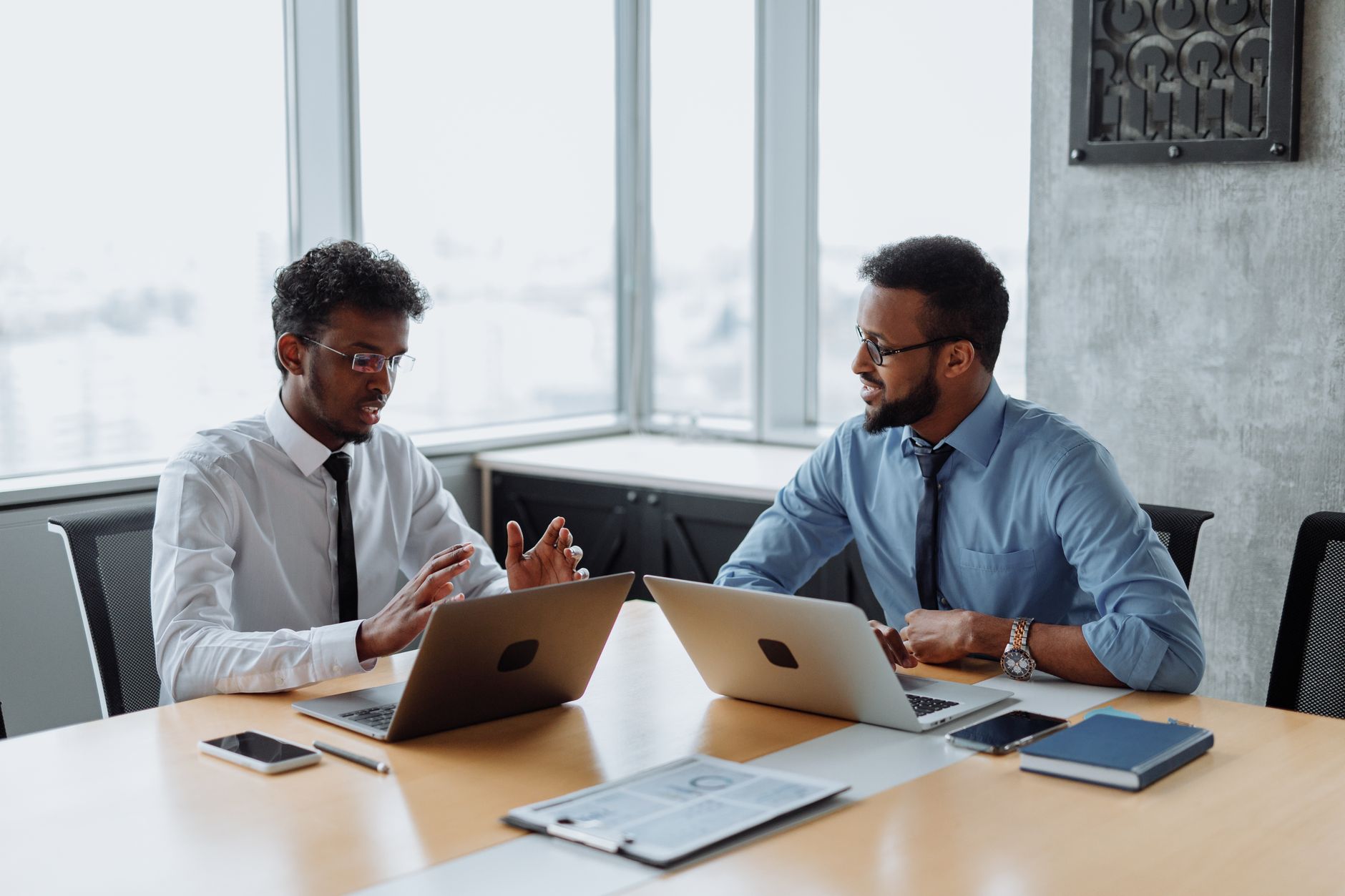 Two African American professionals discussing a project in an office with laptops.